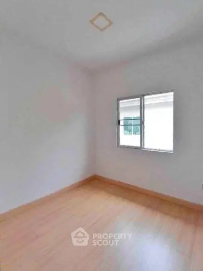 Minimalist empty room with wooden flooring and bright window view.