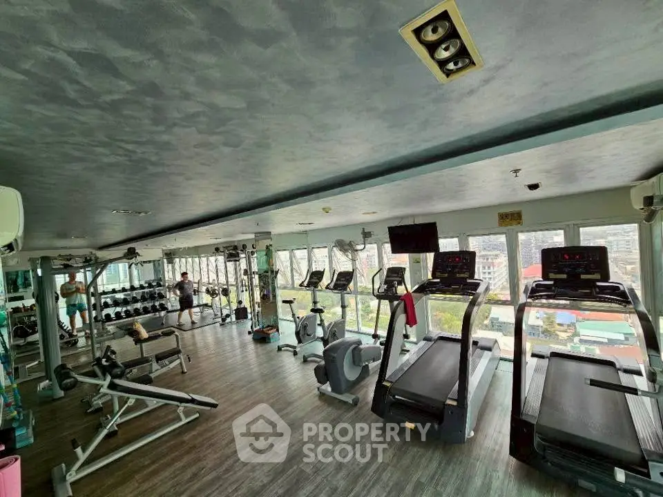 Spacious gym with modern equipment and city view, perfect for fitness enthusiasts.