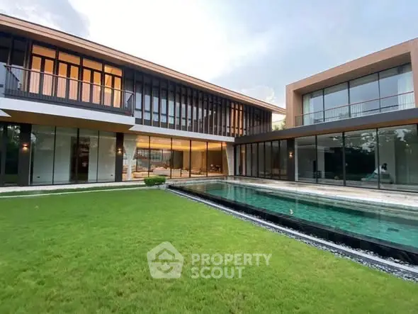 Luxurious modern home with expansive glass windows and private pool, surrounded by lush green lawn.