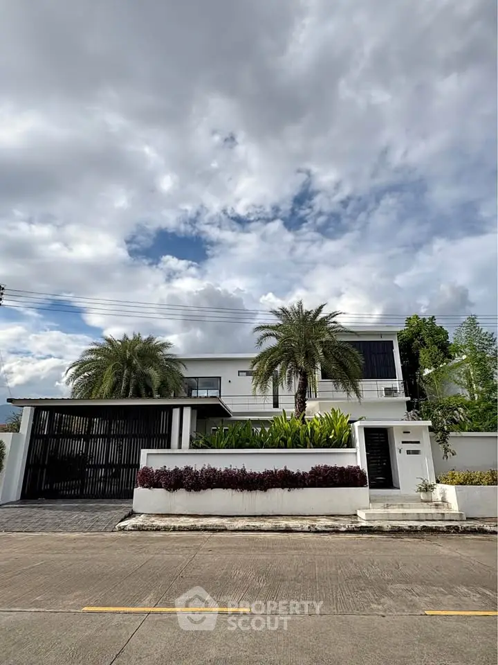 Modern two-story house with lush landscaping and palm trees under a cloudy sky.