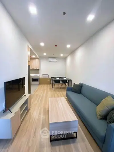 Modern living room with sleek furniture and open layout, featuring a cozy sofa and flat-screen TV.