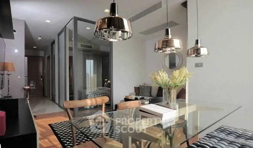 Modern open-plan living and dining area with stylish lighting and glass table.