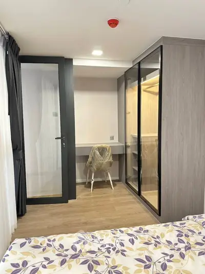 Modern bedroom with glass wardrobe and study area, featuring elegant decor and natural light.
