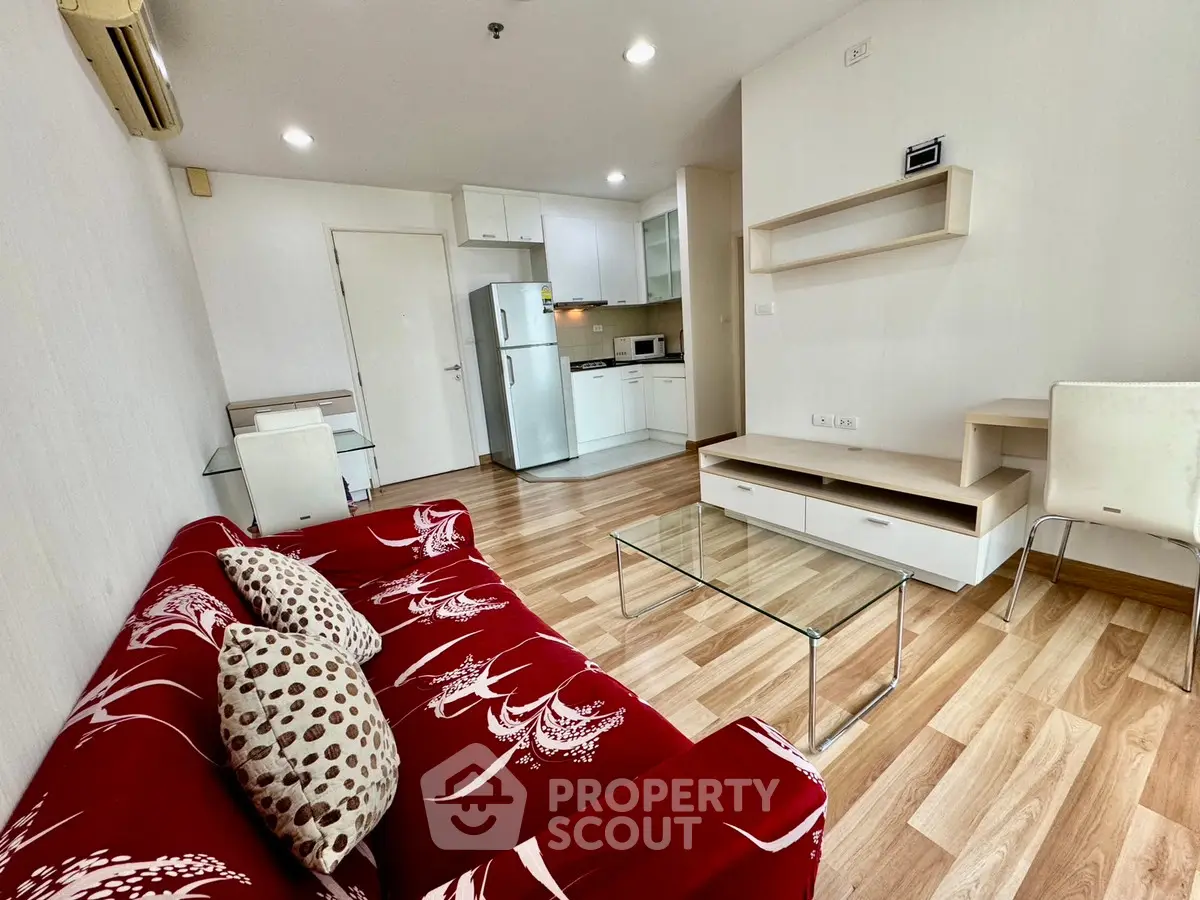 Modern living room with red sofa and open kitchen layout, featuring sleek wooden flooring.