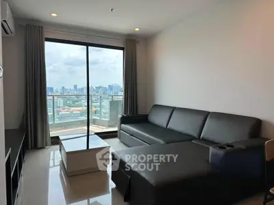 Modern living room with city view, featuring sleek black sofa and large windows for natural light.
