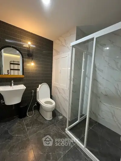 Modern bathroom with sleek design, featuring a glass shower enclosure and stylish black tile accents.