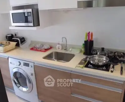 Modern kitchen with washing machine, microwave, and gas stove in sleek apartment.