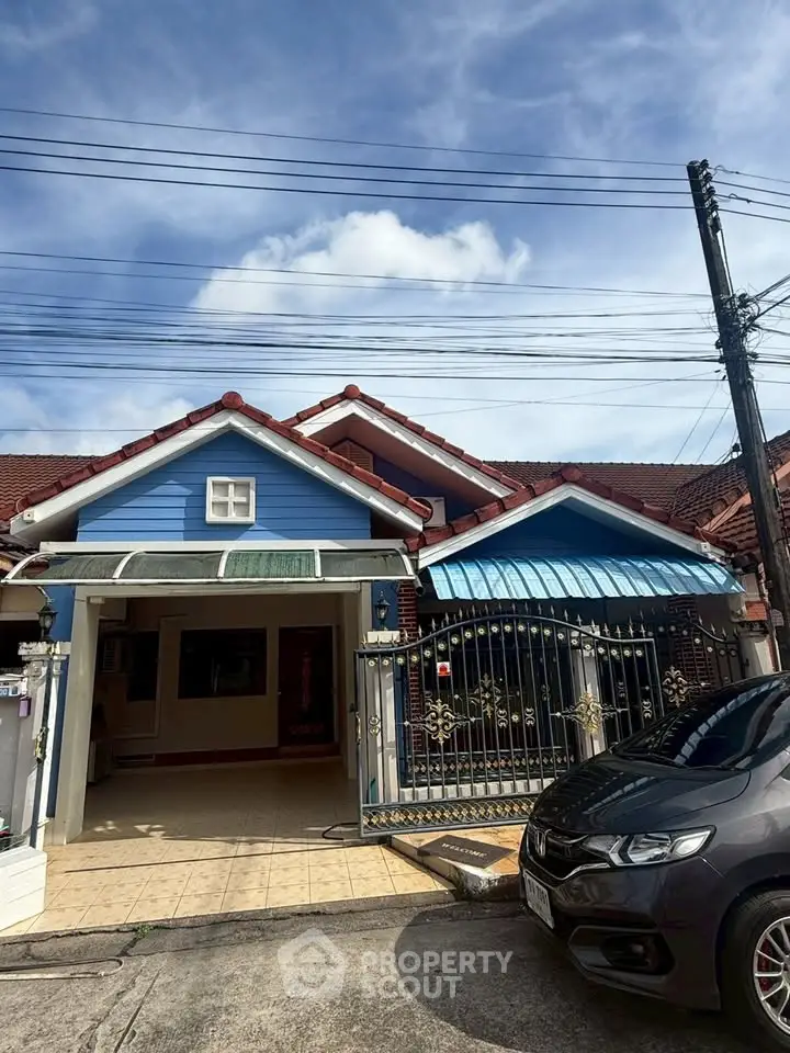Charming suburban house with blue facade and gated entrance under a clear sky.