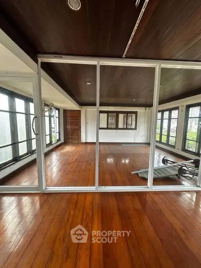 Spacious wooden-floored room with large windows and sliding glass doors, perfect for versatile living space.