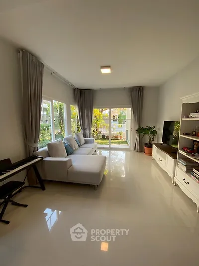 Spacious living room with large windows and garden view, featuring modern furniture and natural light.
