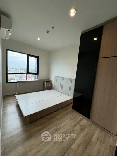Modern bedroom with large window and wooden flooring, featuring a sleek wardrobe and minimalist design.