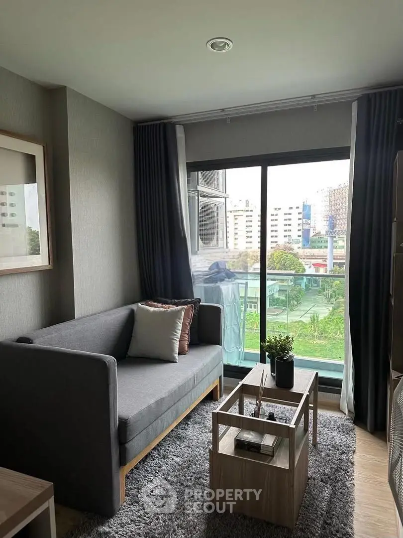 Modern living room with gray sofa, stylish decor, and city view from balcony.