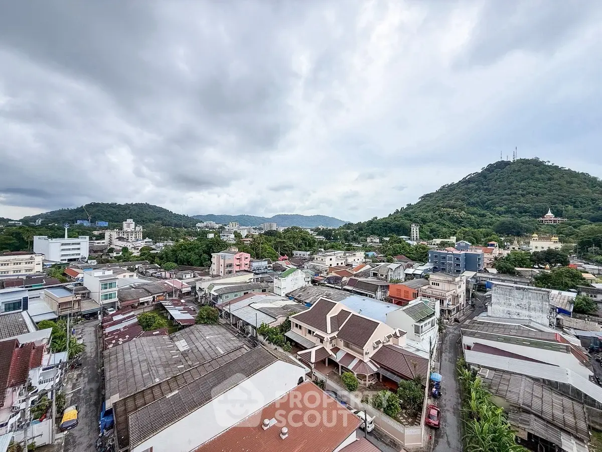 Scenic aerial view of urban landscape with lush hills and residential buildings under cloudy sky.