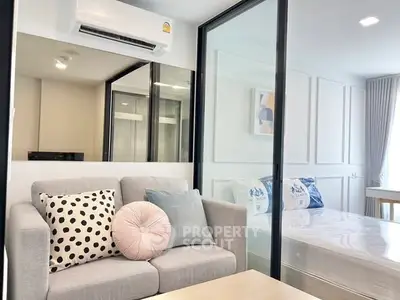 Modern living room with stylish decor and adjacent bedroom separated by glass partition.