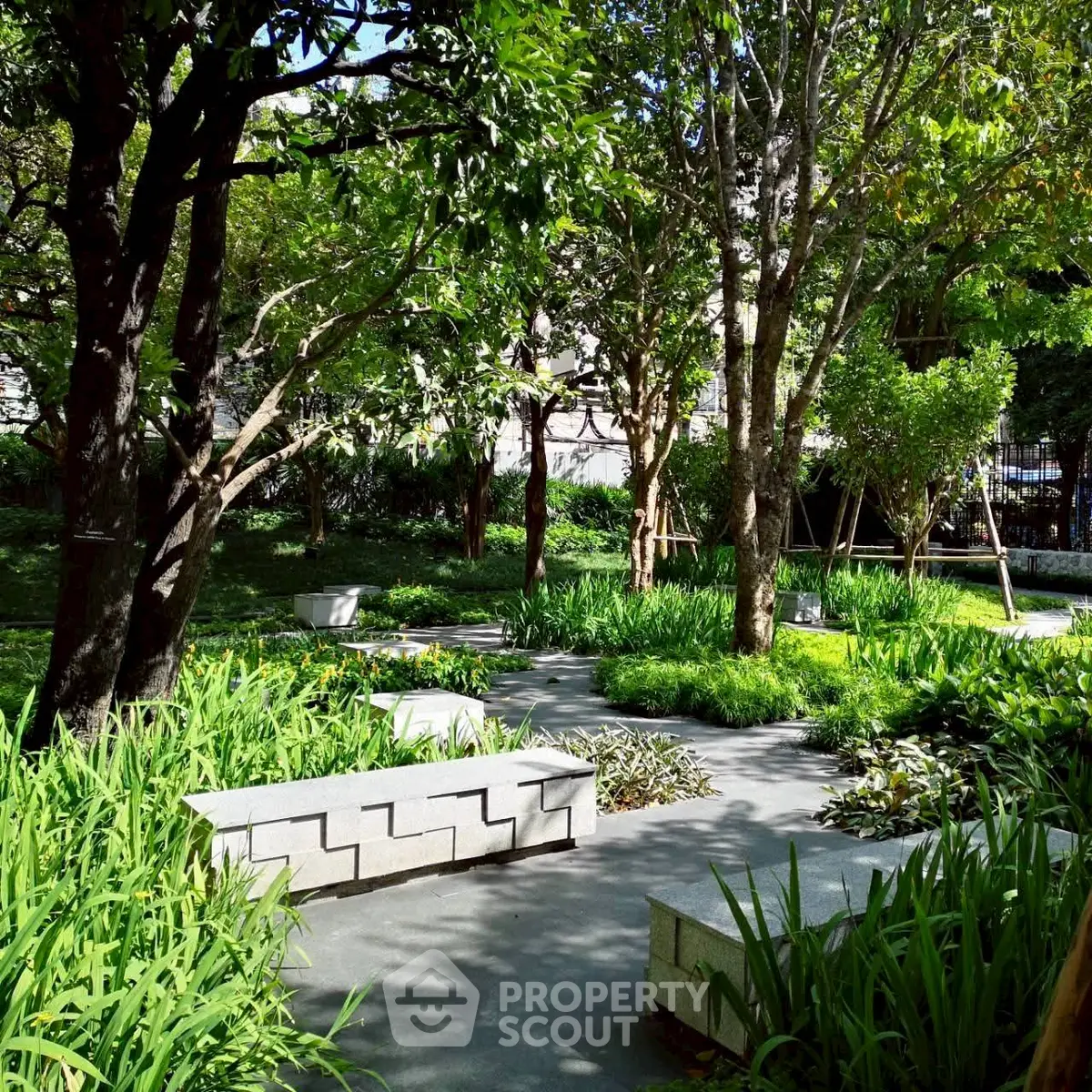 Serene garden with lush greenery and stone benches in a residential complex.
