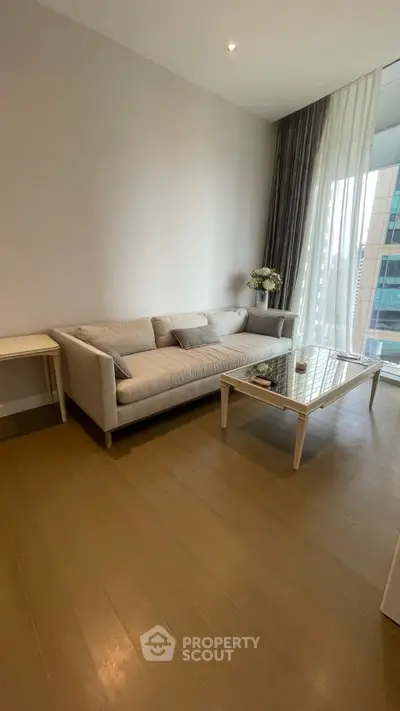 Modern living room with sleek sofa and glass coffee table, featuring floor-to-ceiling windows and elegant decor.