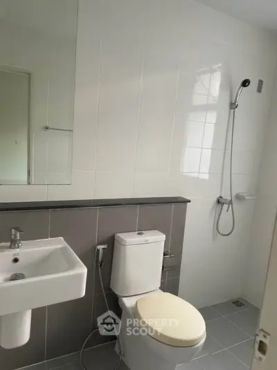 Modern bathroom with sleek fixtures and neutral tiles, featuring a shower and toilet.