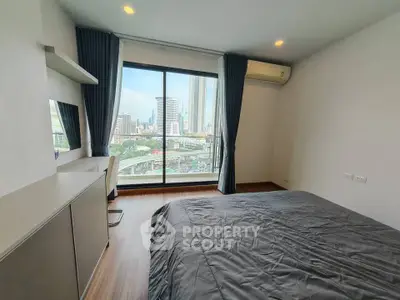 Modern bedroom with city view, featuring large window and sleek furnishings.
