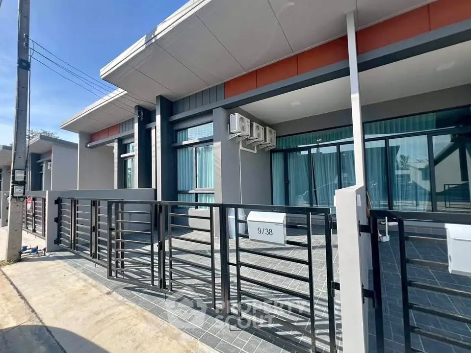 Modern single-story house with sleek design and large windows, featuring a gated front entrance and air conditioning units.