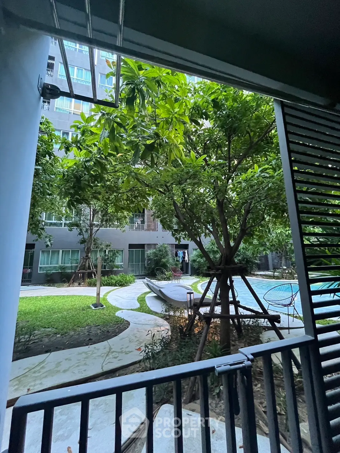 Charming garden view from balcony with lush greenery and pool in modern residential complex.