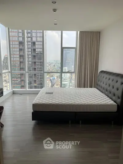 Spacious bedroom with floor-to-ceiling windows offering stunning city views in a modern high-rise apartment.