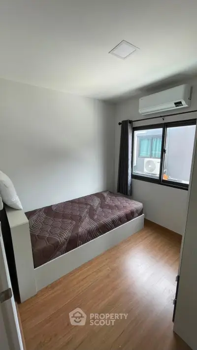 Cozy bedroom with single bed, air conditioning, and wooden flooring, perfect for a minimalist lifestyle.