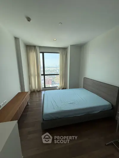 Spacious bedroom with large window offering stunning city views, featuring modern furnishings and natural light.