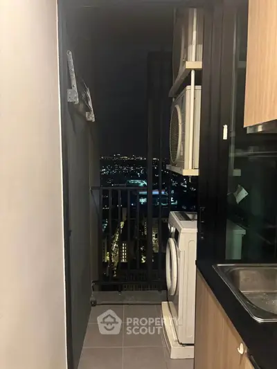 Modern apartment balcony with city view and laundry appliances at night.