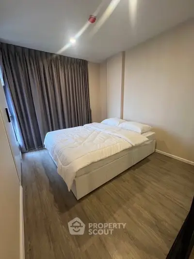 Cozy bedroom with modern decor and wooden flooring, featuring a comfortable bed and elegant curtains.