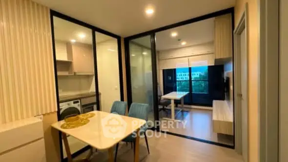 Modern open-layout apartment with dining area and glass partitions, featuring sleek furniture and bright lighting.