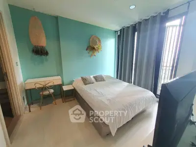 Modern bedroom with teal accent wall and natural light, featuring stylish decor and cozy ambiance.