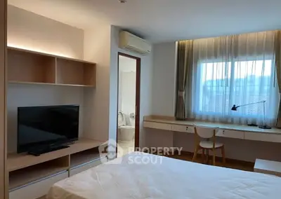 Modern bedroom with TV, desk, and large window offering natural light.