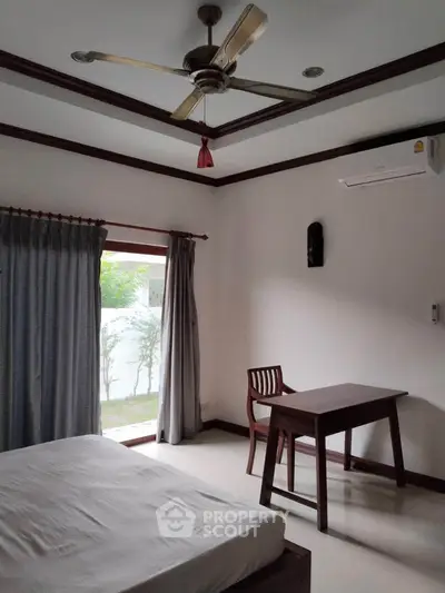 Cozy bedroom with wooden furniture and garden view, featuring a ceiling fan and air conditioning.