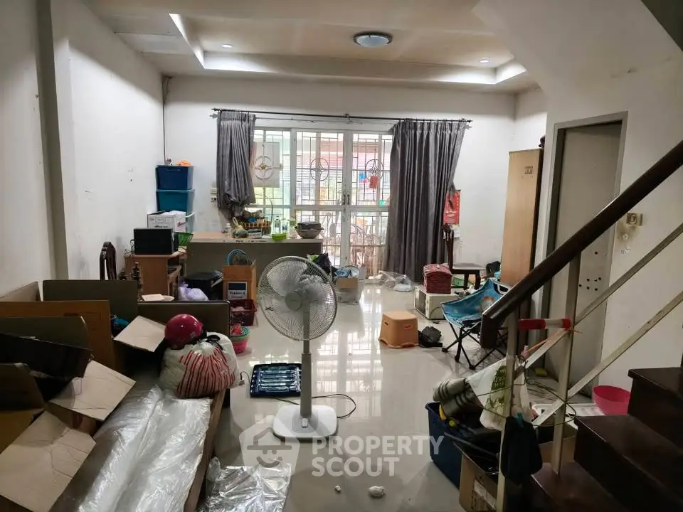 Spacious living room with potential, featuring large window and staircase, ideal for renovation.