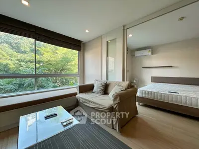 Modern living room with large window and cozy sofa, adjacent to a bedroom with natural light.