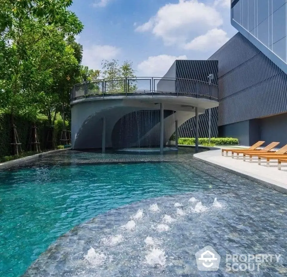 Luxurious private pool with integrated jacuzzi under a modern curved overhang, surrounded by lush greenery and sleek loungers, adjacent to a contemporary residence.