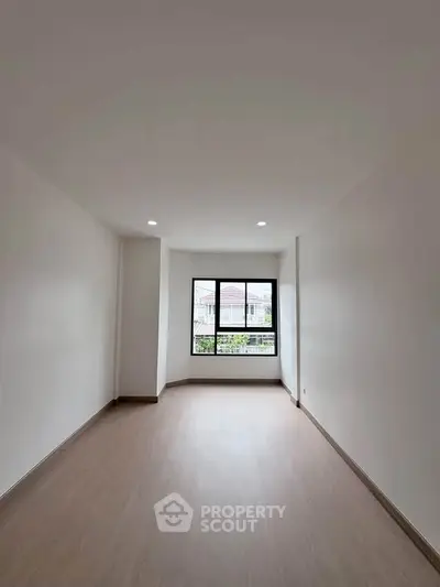 Spacious empty room with large window and wooden flooring, perfect for customization.