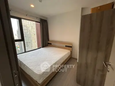 Modern bedroom with large window and city view, featuring a minimalist wooden bed frame and comfortable mattress.