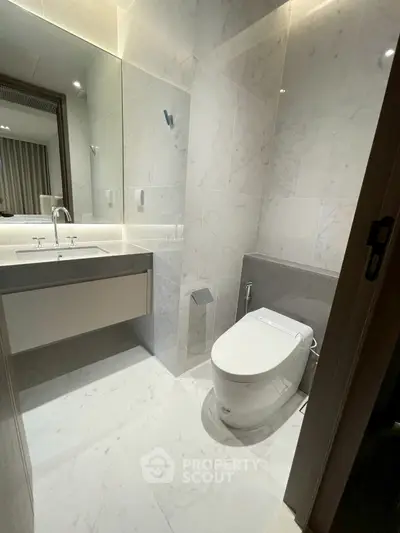 Modern bathroom with sleek fixtures and marble tiles, featuring a contemporary toilet and large mirror.