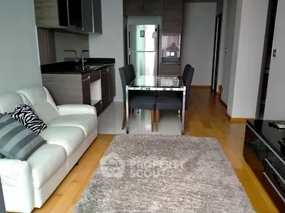 Modern open-layout living room with kitchen, featuring sleek furniture and hardwood floors.
