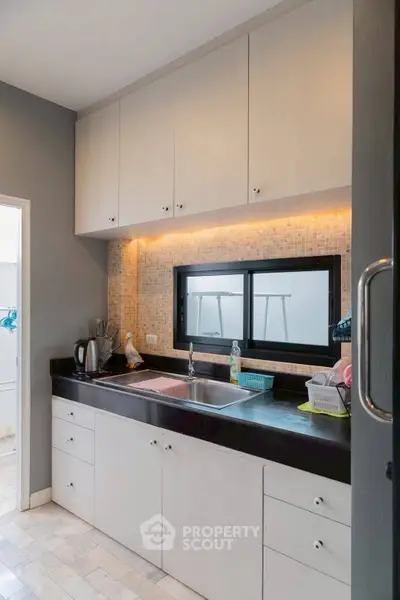 Modern kitchen with sleek cabinetry and under-cabinet lighting, featuring a double sink and stylish backsplash.