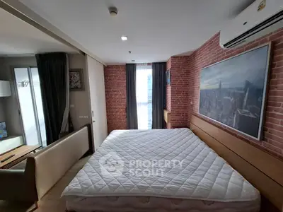 Spacious bedroom with brick accent wall and cityscape artwork, featuring a large window for natural light.