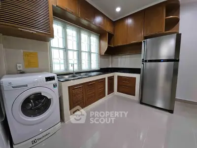 Modern kitchen with wooden cabinets, washing machine, and stainless steel fridge.