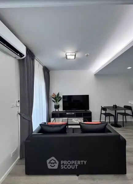 Modern living room with sleek black sofa, TV, and dining area, perfect for urban living.