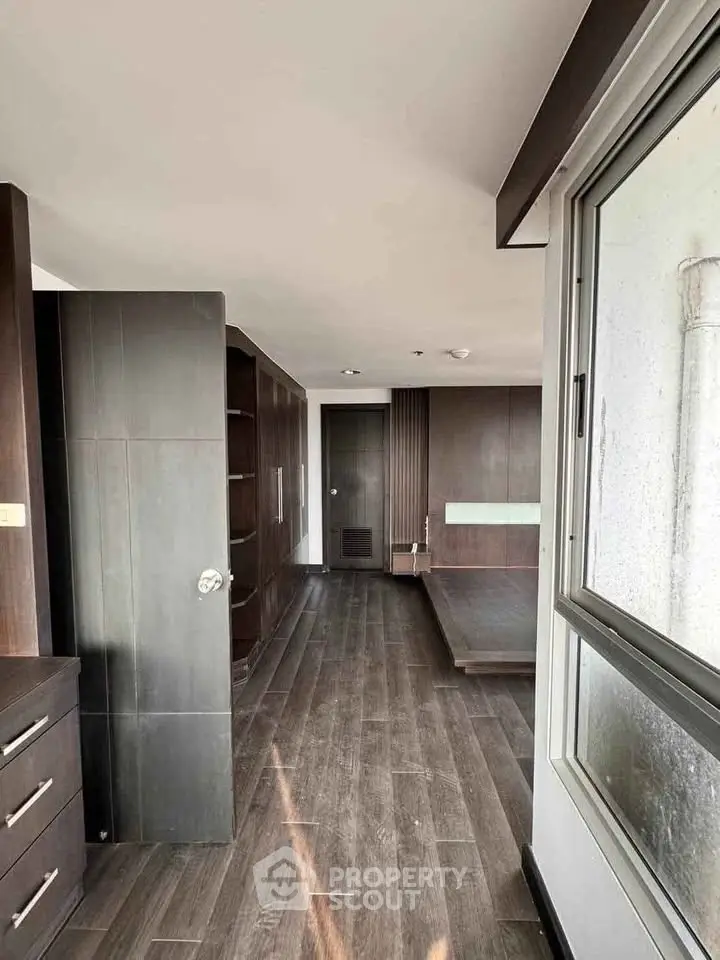 Spacious modern bedroom with wooden flooring and large window offering natural light.