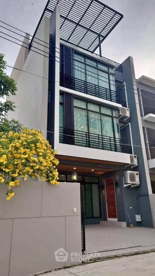 Modern three-story townhouse with sleek design and vibrant yellow flowers in front yard.