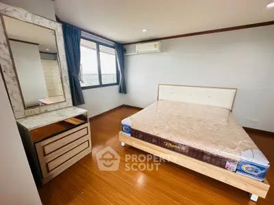 Spacious bedroom with wooden flooring and large window offering natural light.