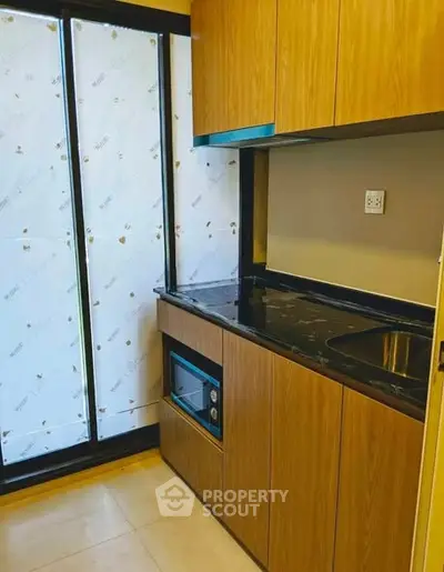 Modern kitchen with sleek wooden cabinets and black countertop, featuring built-in microwave and large window.