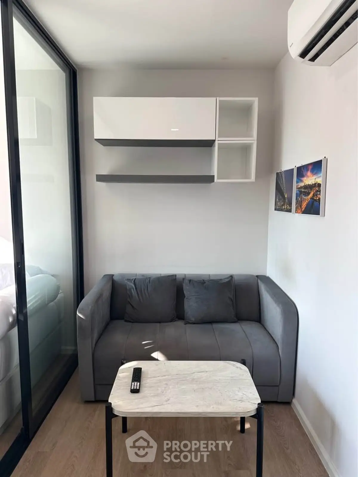 Modern living room with sleek gray sofa, wall-mounted shelves, and air conditioning unit.