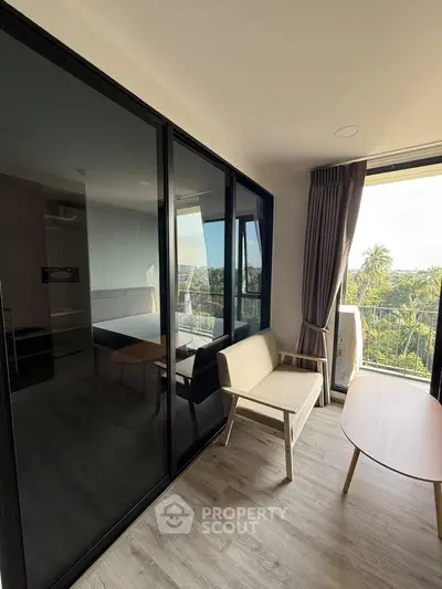 Modern living room with balcony and scenic view, featuring sleek furniture and large glass doors.